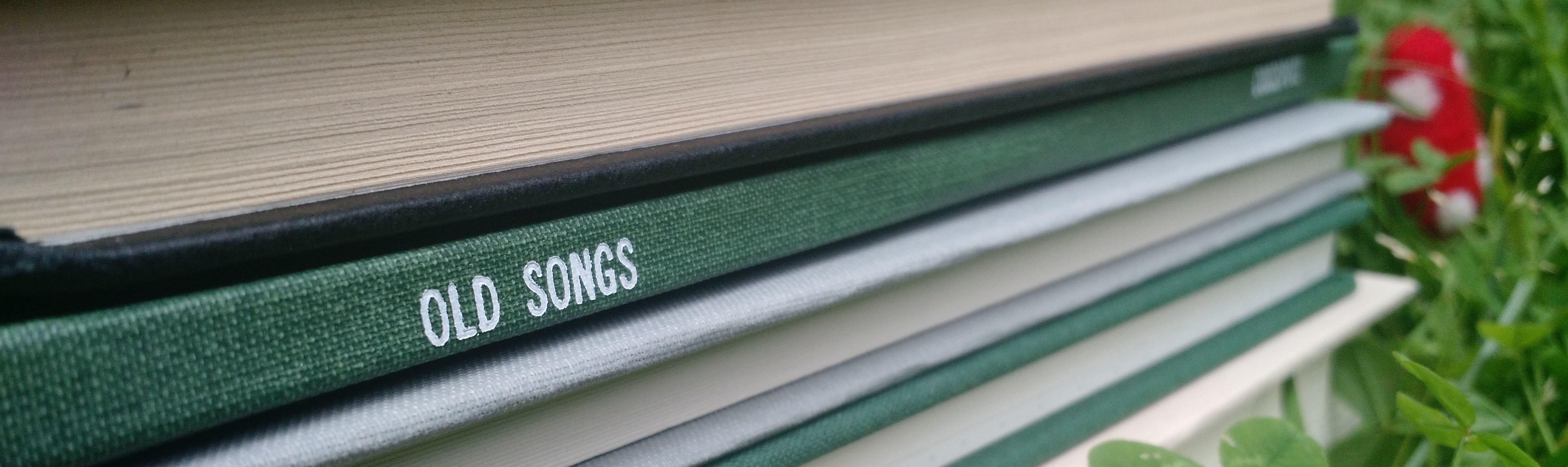 a picture of the spine of Old Songs in a stack of books, with clover and a toadstool in the background